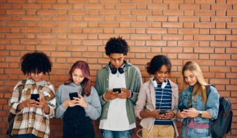 Cinco jóvenes, personificación de la generación incomunicada, están de pie frente a una pared de ladrillos, absortos en sus teléfonos inteligentes.
