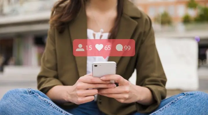 Una persona sentada con las piernas cruzadas al aire libre usa un teléfono inteligente, con íconos de notificaciones de redes sociales para seguidores, me gusta y comentarios que se muestran encima del dispositivo, lo que ilustra las mentiras del social media.