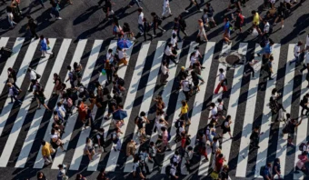 Vista aérea de un cruce peatonal lleno de gente con muchas personas caminando en diferentes direcciones sobre líneas anchas de rayas blancas, lo que ilustra un objetivo potencial para el INEGI para estudios de población urbana.