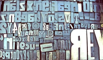 Una colección de bloques tipográficos de metal surtidos dispuestos en una cuadrícula, que muestran la tipografía con varias fuentes, tamaños y orientaciones.