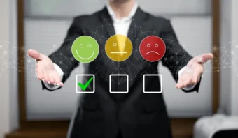 Una persona con traje se encuentra detrás de tres Ãconos que muestran caras felices, neutrales y tristes (como opciones en una encuesta de servicio) con una marca de verificación verde debajo de la cara feliz.