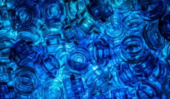 Una vista de cerca de muchas tapas de botellas azules translúcidas, que muestran el azul mientras están dispersas y apiladas juntas, bellamente iluminadas desde abajo.