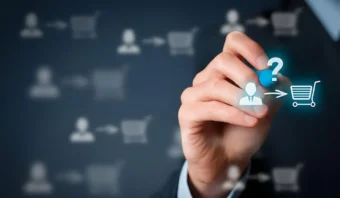 Una mano sostiene un marcador azul, dibujando íconos de una persona, un signo de interrogación y un carrito de compras, que simbolizan la toma de decisiones del cliente en el comercio electrónico y el marketing de consumo tradicional sobre un fondo de interfaz digital borroso.
