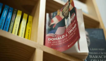 Una estantería con diversos libros, incluida una edición vietnamita de un libro de Trump expuesta de forma destacada.