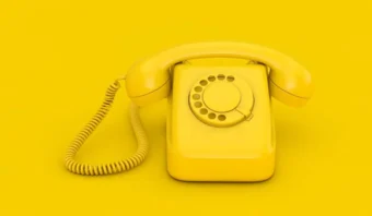 Un teléfono de disco amarillo con un cable enrollado se encuentra sobre una superficie y un fondo amarillos, celebrando el amarillo en una escena vibrante y monocromática.
