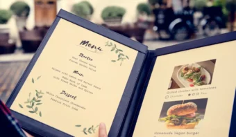 Una persona sostiene un menú contemporáneo con un entrante, un plato principal y un postre en la página izquierda, con fotos y descripciones de los platos en la página derecha.