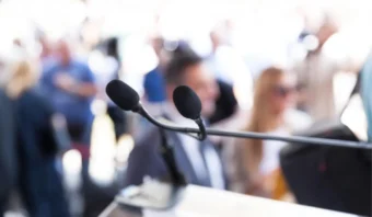 Dos micrófonos están posicionados en un soporte con una multitud borrosa en el fondo, creando una escena dinámica que a menudo se encuentra en eventos de mercadotecnia política.