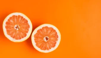 Dos mitades de pomelo con pulpa rosada se colocan una al lado de la otra sobre un fondo sólido de color naranja.