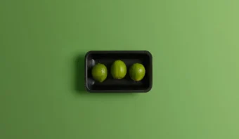 Tres limas reposan en una bandeja negra sobre un fondo verde, resaltando su vibrante frescura.