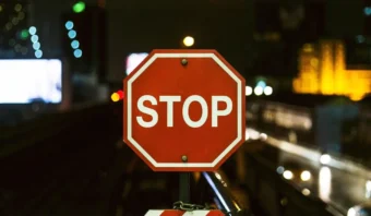 Una seÃ±al de pare octogonal de color rojo se muestra de noche con luces de la ciudad y edificios borrosos en el fondo, evocando sutilmente la idea de los pecados capitales de Internet y recordÃ¡ndonos que debemos hacer una pausa antes de cruzar los lÃ­mites digitales.