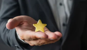 Una persona con traje sostiene en su mano abierta un objeto dorado en forma de estrella, simbolizando el reconocimiento a un programa de lealtad exitoso, con el foco puesto en la estrella y la mano.