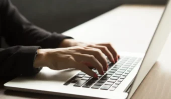 Primer plano de las manos de una persona escribiendo en un teclado portátil sobre un escritorio de color claro, capturando el momento justo antes de que se enfocara.