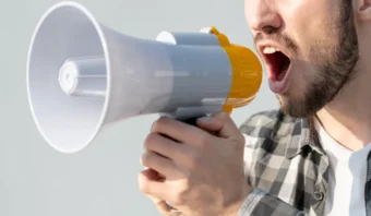 Un hombre con un megáfono cerca de la boca grita o habla a través de él: una imagen impactante para los Community Managers que buscan imágenes que llamen la atención. El fondo es simple, destacando su expresión y el megáfono.