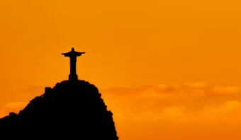 Silueta de la estatua del Cristo Redentor en lo alto de una colina contra un cielo naranja al atardecer, que recuerda las imágenes icónicas de Río 2016.
