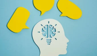 Recorte de papel de una cabeza con un cerebro representado como una bombilla, rodeada de tres burbujas de diálogo amarillas sobre un fondo azul, que simboliza el conocimiento como estrategia de venta.