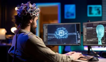 Una persona que lleva un casco de monitorización de ondas cerebrales se sienta en un escritorio y utiliza una computadora con pantallas que muestran gráficos cerebrales relacionados con el neuromarketing y la inteligencia artificial.