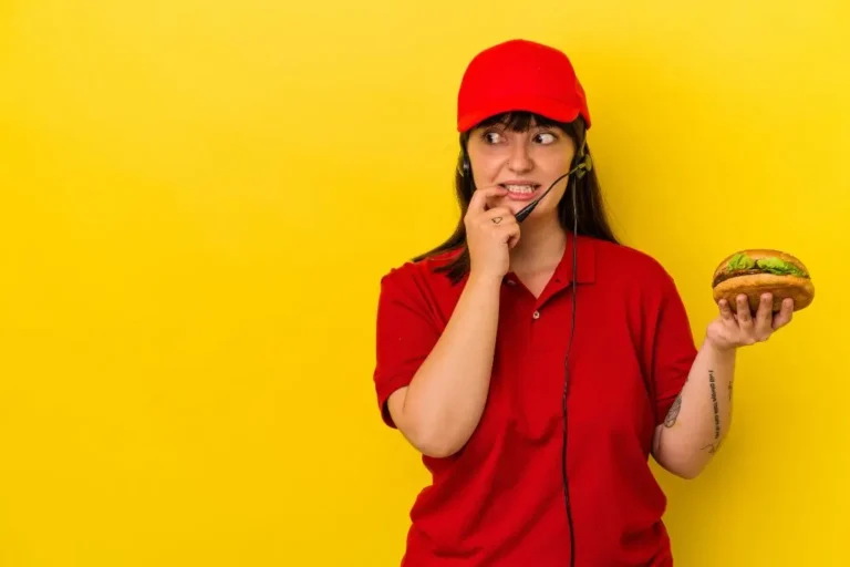 Una mujer con uniforme rojo y auriculares sostiene una hamburguesa y mira nerviosamente hacia un lado sobre un fondo amarillo, perfecto para las imágenes de Contenido Fast Food.