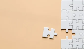 Un rompecabezas blanco parcialmente terminado sobre una superficie beige, con una pieza separada, ilustra la estrecha relaciÃ³n entre marketing y ventas, ambos esenciales para completar el panorama mÃ¡s amplio de cualquier estrategia comercial.