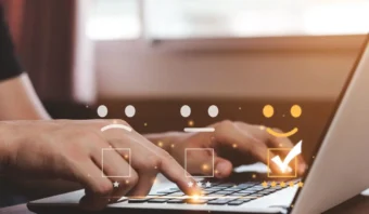 Una persona usa una laptop con íconos de calificación (caras tristes, neutrales y felices) sobre el teclado. La cara feliz está marcada, lo que refleja satisfacción vs. lealtad en los comentarios de los clientes.