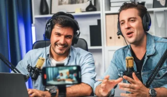 Dos hombres con auriculares hablan por micrÃ³fonos y estÃ¡n sentados en un escritorio con una computadora portÃ¡til, grabando un podcast o una transmisiÃ³n en vivo en un estudio moderno, discutiendo el negocio de los YouTubers.