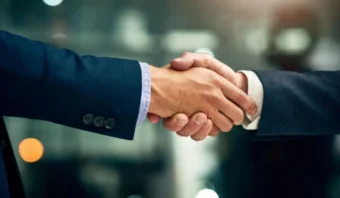 Dos personas vestidas con trajes de negocios se dan la mano en un entorno profesional, simbolizando la lealtad de los clientes, con un fondo borroso.