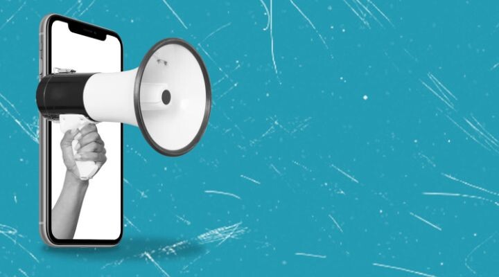 Una mano que sostiene un megáfono emerge de la pantalla de un teléfono inteligente sobre un fondo azul texturizado, simbolizando el poder de la comunicación digital para quienes eligen trabajar como autónomos muestra que es ser freelance.