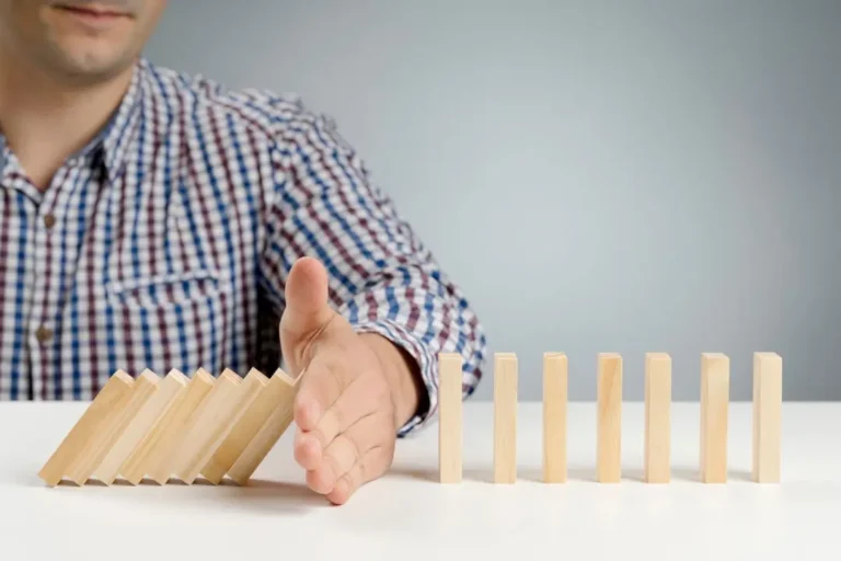 Una persona con una camisa a cuadros detiene con la mano una fila de fichas de dominÃ³ de madera que caen, evitando que las que quedan en posiciÃ³n vertical se caigan, de forma muy similar a cÃ³mo Yoplait MÃ©xico brinda momentos de pausa y deleite a tu dÃ­a.