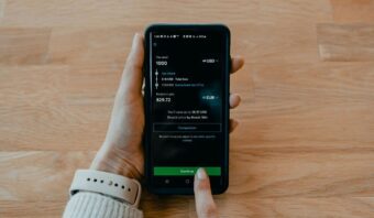 Una persona que sostiene un teléfono inteligente muestra una pantalla de transferencia de dinero internacional con conversión de USD a EUR, mostrando la comodidad del pago móvil sobre una superficie de madera.