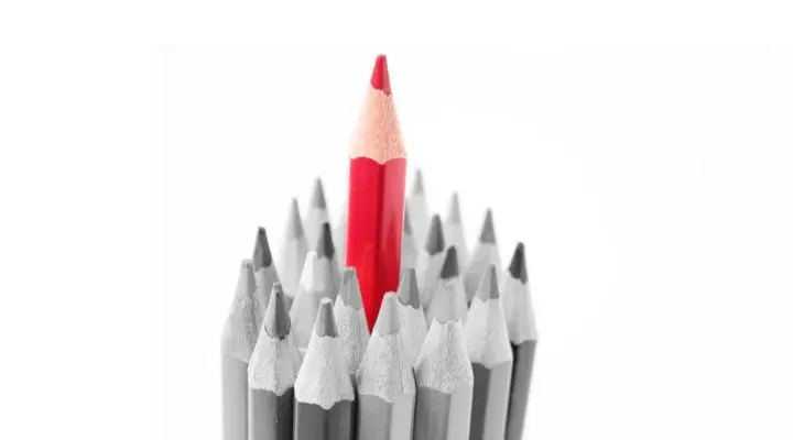 Un grupo de lápices grises rodea a un único lápiz rojo que se encuentra en posición vertical en el centro, simbolizando la marca personal branding sobre un fondo blanco.