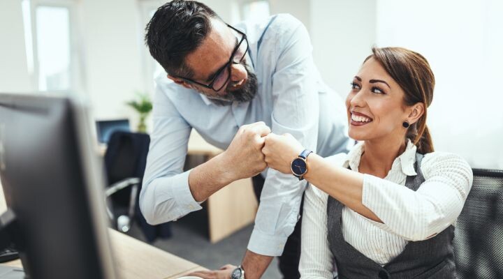 Un hombre y una mujer en una oficina sonrÃen y chocan los puños Reposiciónate en el 2017