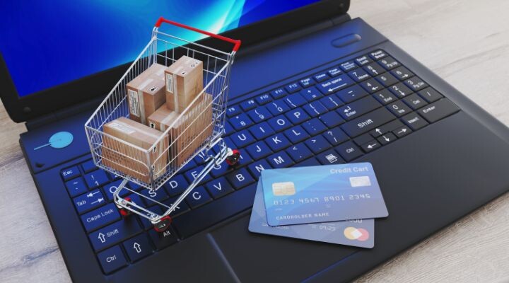 Un carrito de compras con cajas se coloca sobre el teclado de una computadora portátil, junto a dos tarjetas de crédito. e-commerce