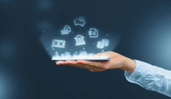 Una mano sostiene un teléfono inteligente con íconos bancarios digitales brillantes (como un banco, monedas, una alcancía, un candado, un documento y un billete de dólar) proyectados sobre él.