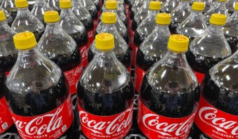 Muchas botellas de coca cola están dispuestas en un estante.