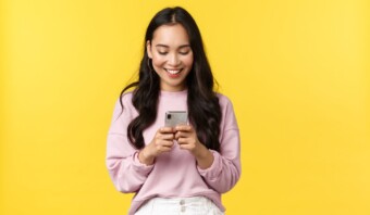 Joven asiÃ¡tica mirando las redes sociales su telÃ©fono inteligente sobre un fondo amarillo.