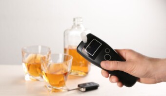 Una persona sosteniendo un alcoholÃ­metro frente a una botella de alcohol.