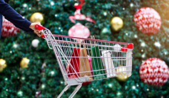 Una mujer sostiene un carrito de compras frente a un árbol de Navidad en medio de una estrategia de marketing navideño.