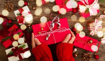 Una mujer sostiene una caja de regalo roja sobre una mesa de madera.