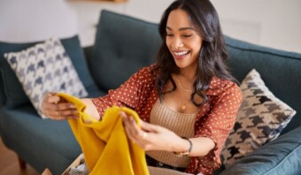 Una mujer está sentada en un sofá y abre una caja de ropa que compró a través de ventas en línea.