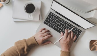 Una persona escribiendo en una computadora portátil con una taza de café.