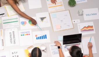 Un grupo de personas trabajando alrededor de una mesa con papeles, colaborando en innovación abierta o formando alianzas exitosas.