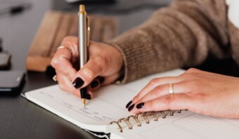 Una mujer escribiendo en un cuaderno con un bolígrafo.