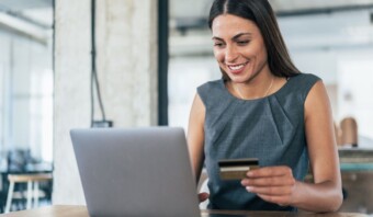 Una mujer sonríe mientras usa una computadora portátil con una tarjeta de crédito.