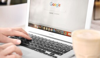 Persona utilizando un macbook con el buscador Google SGE en pantalla, acompañado de una taza de café.