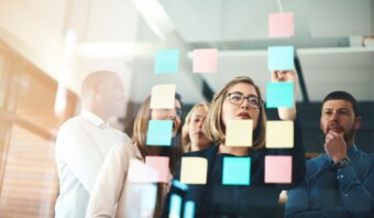 Grupo de profesionales analizando notas adhesivas en una pared de vidrio durante una sesión de lluvia de ideas sobre arte de datos.