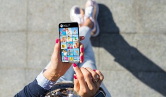 Persona que utiliza un teléfono inteligente para explorar una galería de fotos en redes sociales internas mientras está sentada en el suelo.