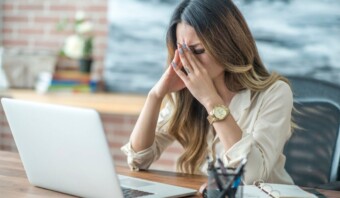 Mujer con estrés laboral y manos en la cara sentada frente a un portátil.