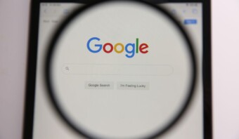 Una lupa enfoca la página de inicio de Google que se muestra en un monitor, resaltando la barra de búsqueda y el logotipo.