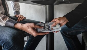 Dos personas sentadas intercambiando impunemente un fajo de billetes de dólares estadounidenses.