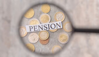 La lupa se centró en varias monedas con una tira de papel con la etiqueta "pensión" colocada encima, sugiriendo el concepto de planificación financiera para la jubilación.