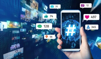 Una mano que sostiene un teléfono inteligente que muestra un símbolo de hashtag, rodeado de pantallas digitales flotantes que muestran varios íconos de redes sociales y números de participación.